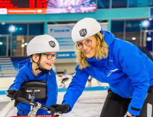 Schaatstrainer Kirsten Muller met een jongen op een schaatsframe.