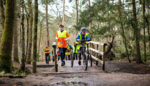 Inclusieve verldloop: atleet op een runningframe rent met andere atleten door een bos.